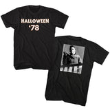 Front and back of Halloween '78 black t-shirt featuring text 'Halloween '78' in white with orange outline on the front and a black and white image of Mike Myers holding a knife on a staircase on the back, displayed against a white background.